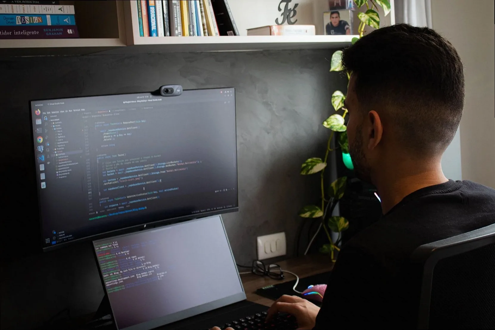 A programmer coding on a laptop and monitor in a stylish office setup.